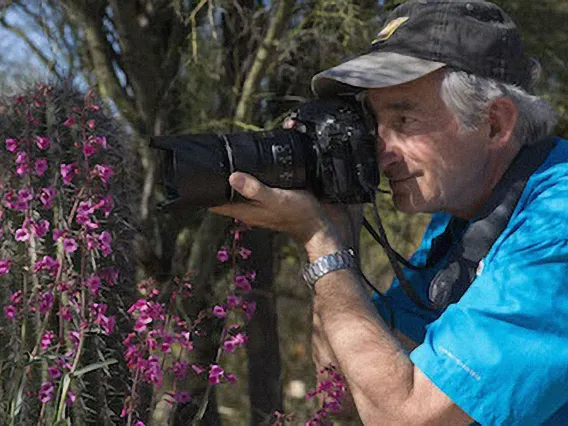 Stephen Buchman in a desert landscape, pointing a camera toward a subject to the left of the frame.