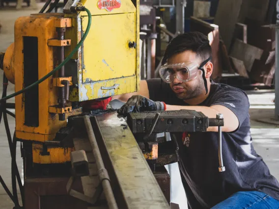 A photo of a CAPLA student cutting a piece of metal for an architecture structure in the materials lab at the college of architecture, planning and landscape architecture