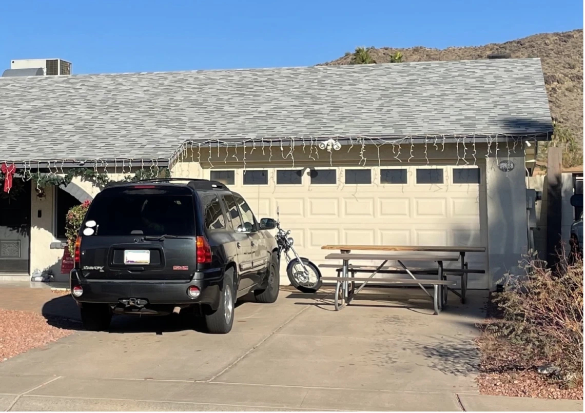 An SUV, motorcycle, and picnic table in the driveway of a single family home with two-car garage.