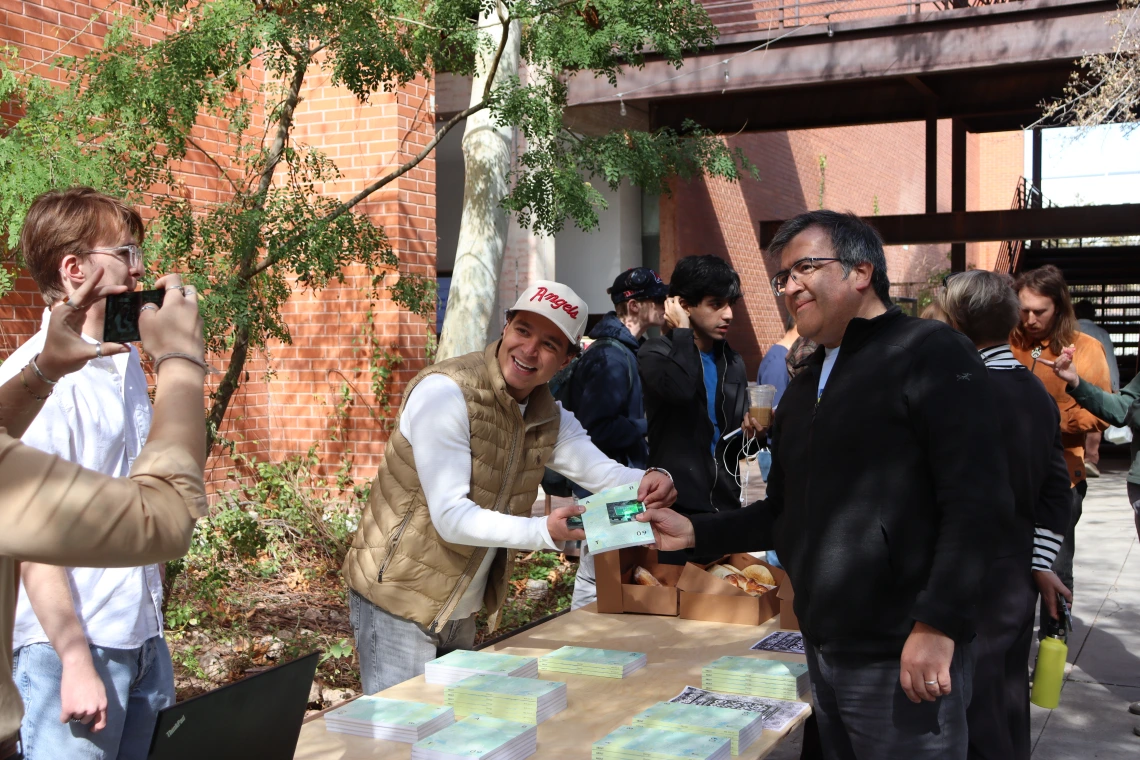 Student poses with a faculty member picking up an issue of the About Journal. 