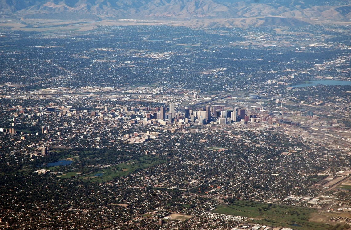 Aerial view of downtown Denver, Colorado, surrounded by suburban sprawl with mountains in the background.