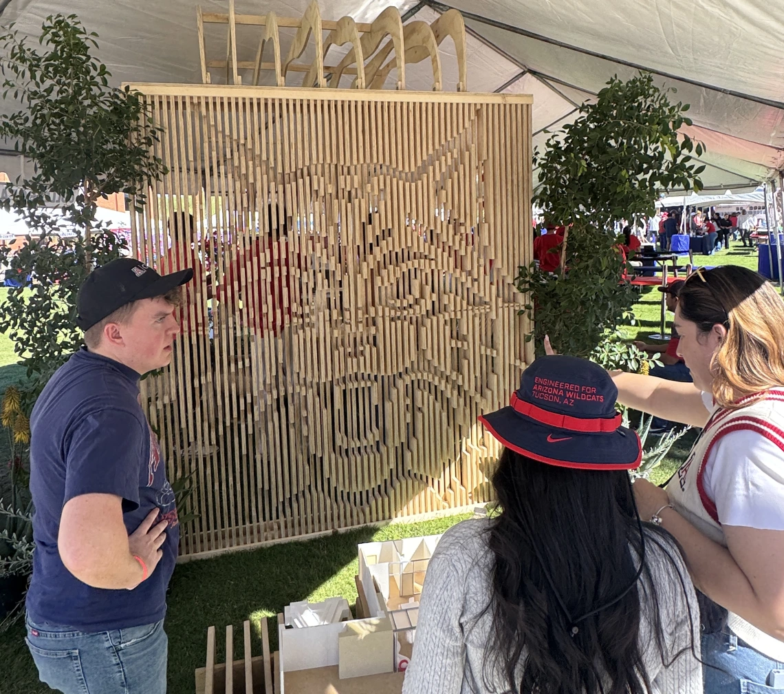 Students gather in front of a wood structure with walls made of slats that create the image of a Wildcat face. 