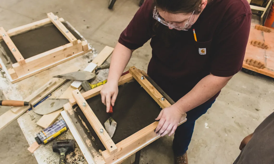 A student smoothing out concrete in the concrete lab at the college of architecture, planning and landscape architecture