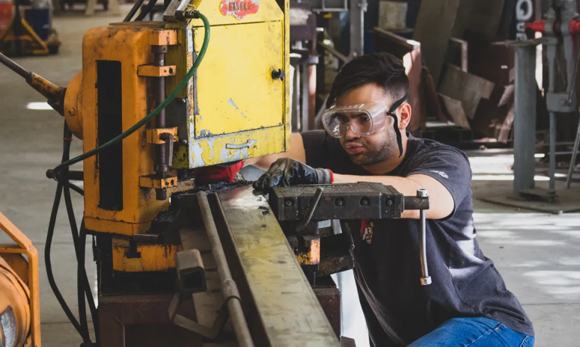 A photo of a CAPLA student cutting a piece of metal for an architecture structure in the materials lab at the college of architecture, planning and landscape architecture