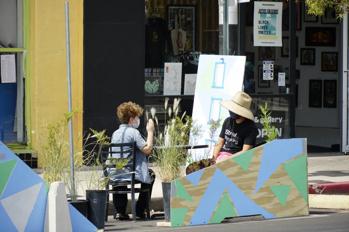 Two people wearing masks sit and talk at an outdoor table in the Parking Day installation.