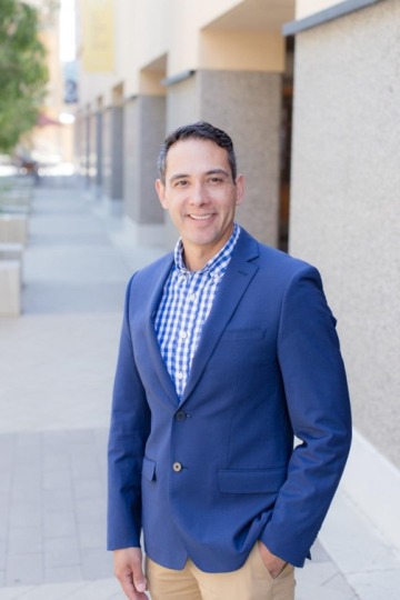 A photo of Michael Mendez wearing a blue blazer outside of an urban office building.
