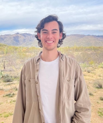 A smiling young white man with the desert landscape as his background. 
