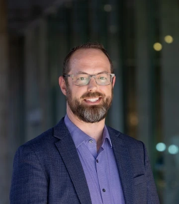 Photo of Ladd Keith, a white man wearing glasses and purple button up and blue coat